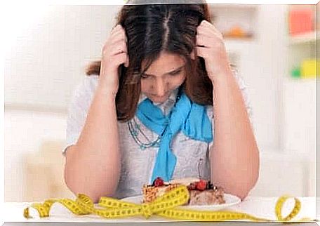 A woman sits with her hands in her hair over a plate of food and a measuring tape