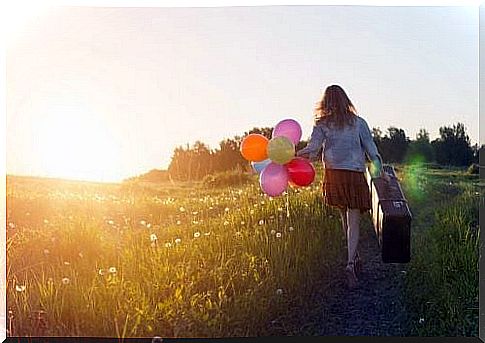 Woman with suitcase and balloons in a field