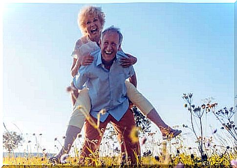 A smiling elderly couple with the woman sitting on the man's back